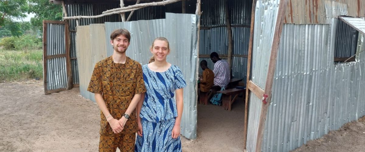 Luke (left) and fellow intern, Elizabeth (right), stand in front of a building made of metal sheets and wood. The building is used as a place of worship and fellowship. 