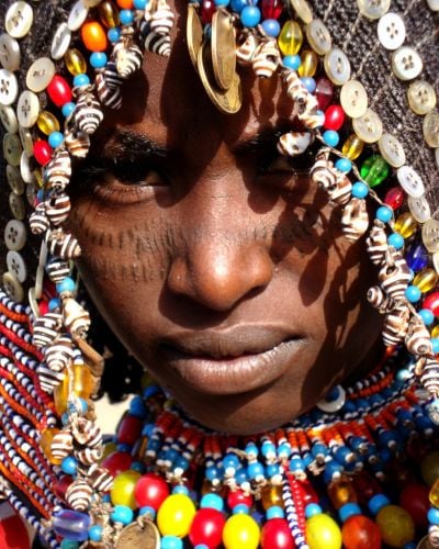An Afar woman peers into the camera from beneath traditional beadwork.
