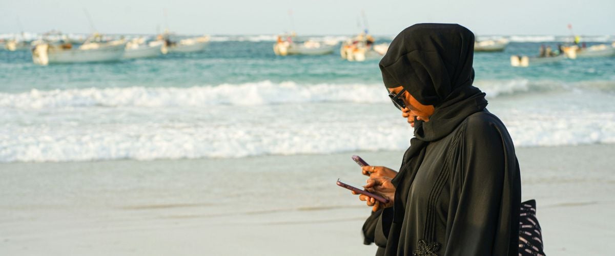 Two women in Somalia walk along the beach with phones in their hands.