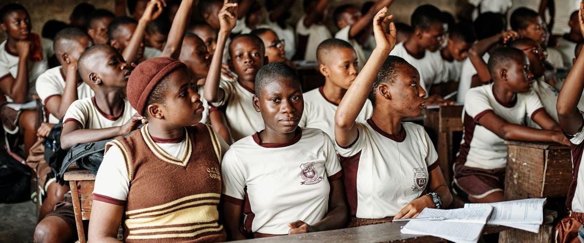 Schoolchildren in Niregia sit at their desks, hands raised to answer their instructor's question.