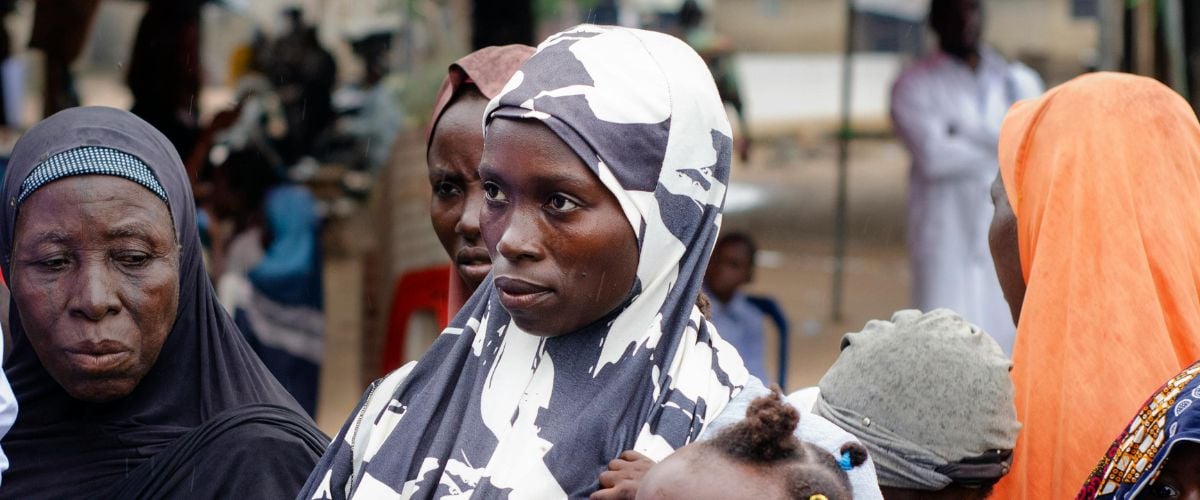 A woman holding a baby stands in a crowd in Nigeria.