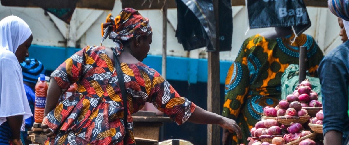 A woman in traditional dress selects produce from a market in Nigeria. 