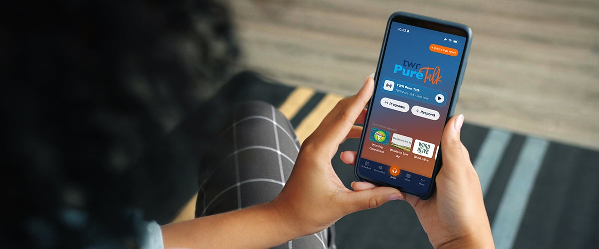 woman holding a phone showing the TWR Pure Talk app open.