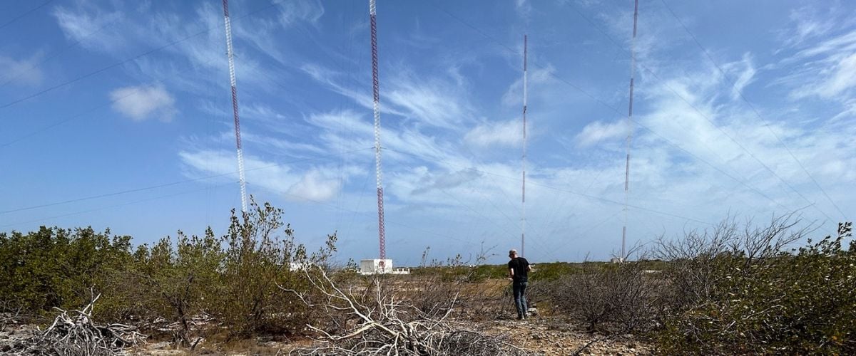 Ryan walks amonst the underbrush of the transmitter field on Bonaire. Four large radio towers can be seen stretching to the sky in the background. 