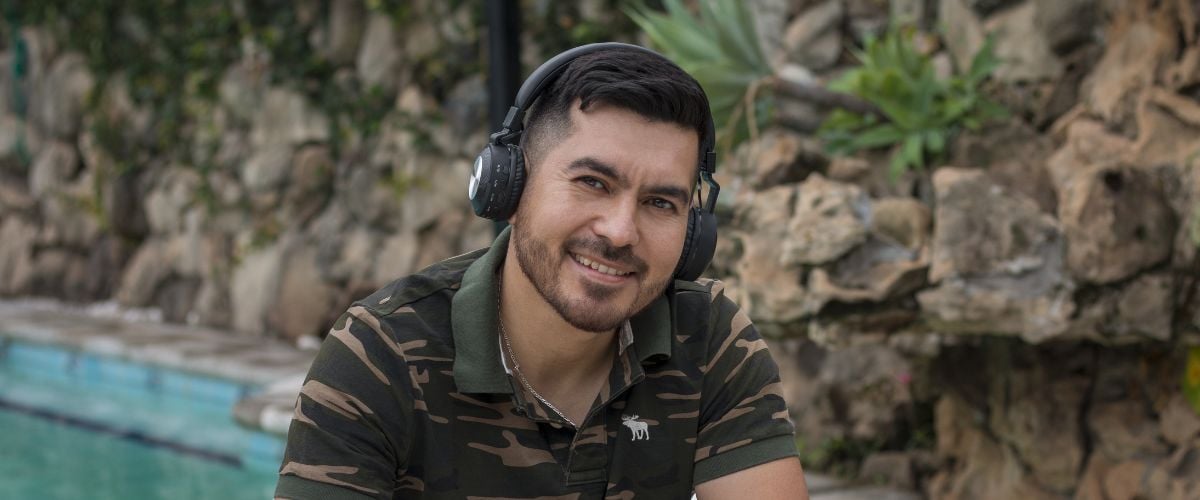 A man from Paraguay looks towards the camera, smiling, while wearing headphones. 
