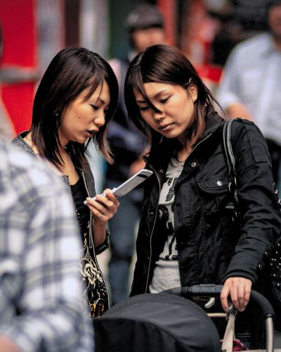 Two young Japanese women look glance at a phone in the streets of Osaka, Japan