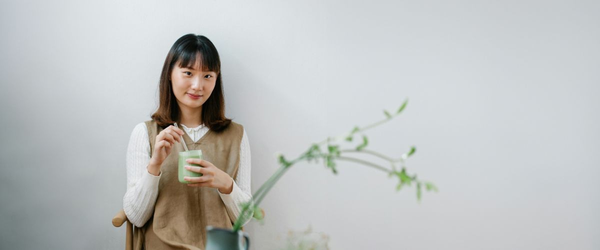 A Japanese woman sits, smiling at the camera while enjoying her tea.