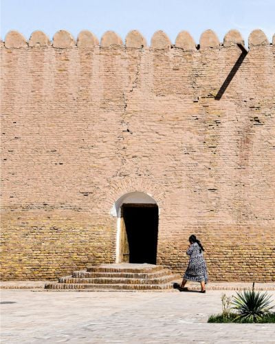 A women in Uzbekistan walks towards a stone doorway.