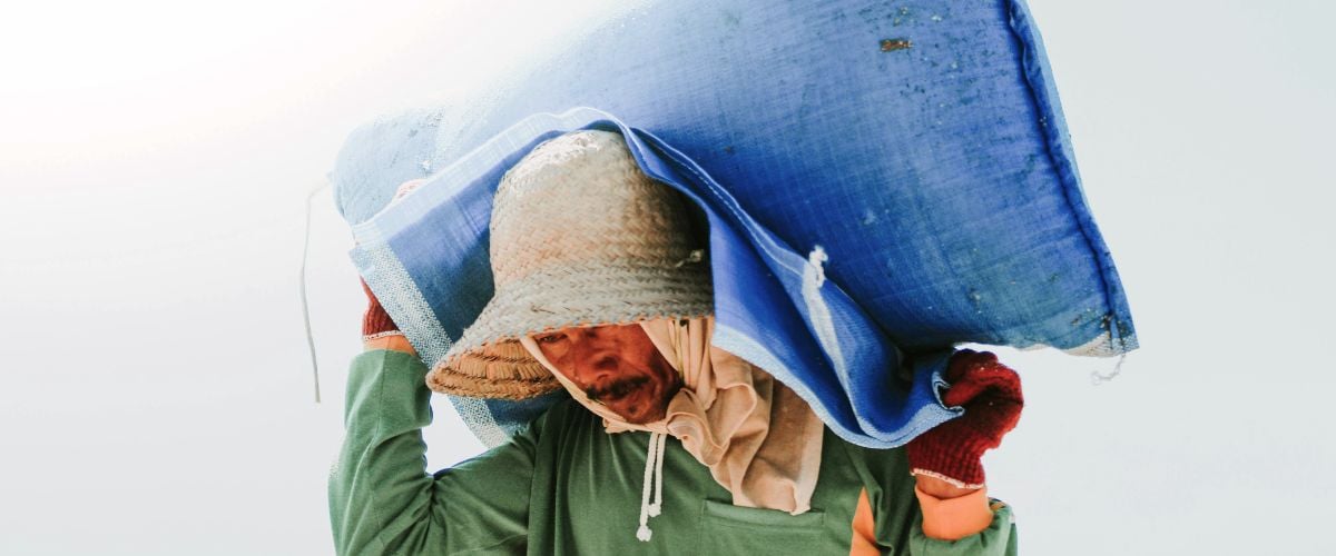 A man in Indonesia carries a heavy bag of grain across his shoulders.