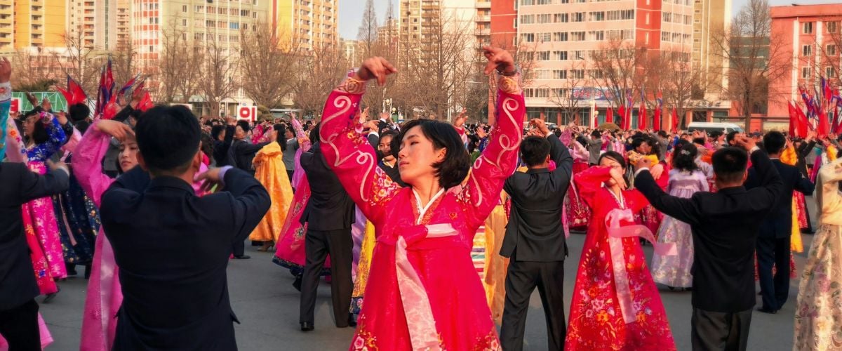 A crowd of people gather to dance in traditional clothing in North Korea.