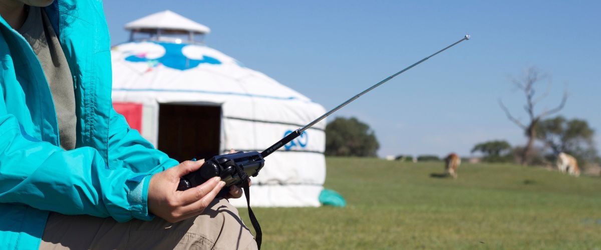 A women in Mongolia tunes into a radio which she holds in her lap. A traditional Mongolian dwelling can be seen in the background. 