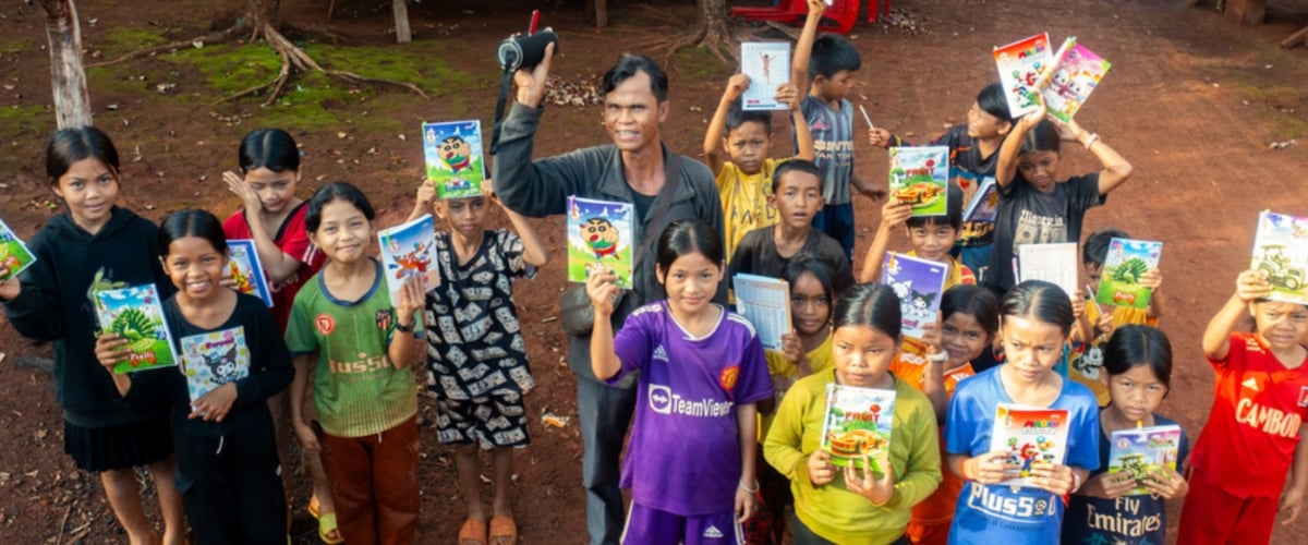 A leader and group of children from the Happy Children's Garden program pose for the camera with their workbooks. 