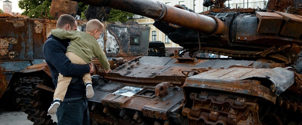 A father holds his son while they observe an old tank in Ukraine.