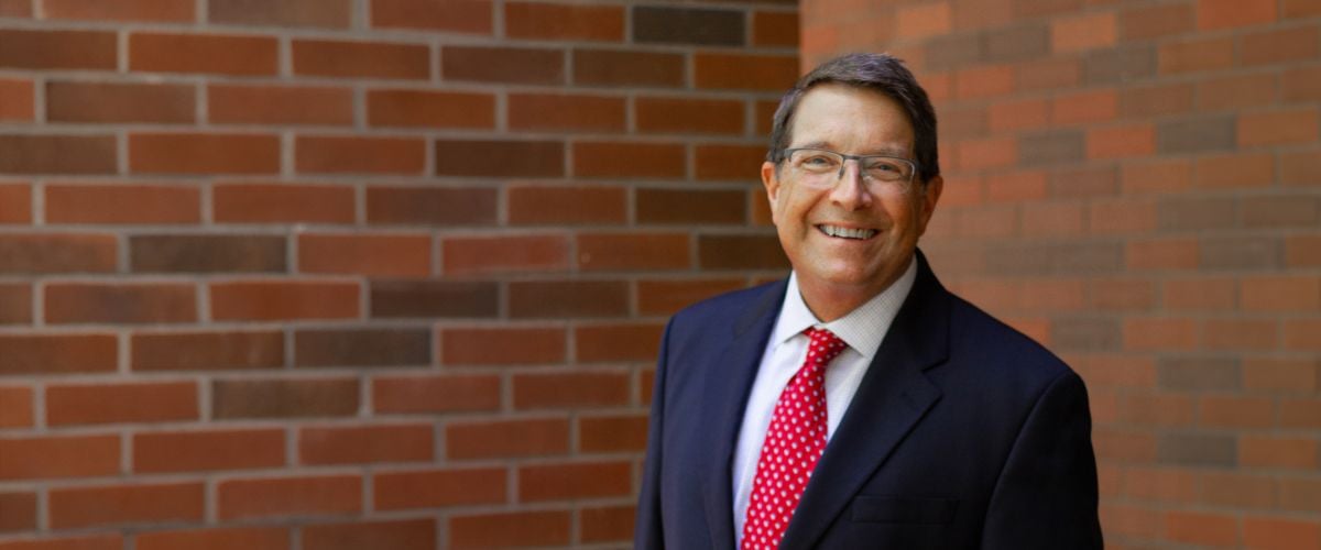 TWR Interim President Cassius Smith stands in front of a brick wall in a blazer and tie.