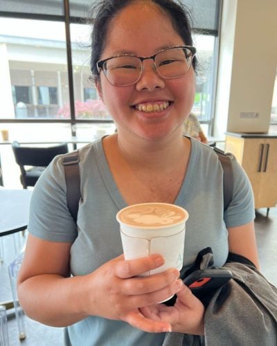 Joanna smiles at the camera with coffe in hand. 