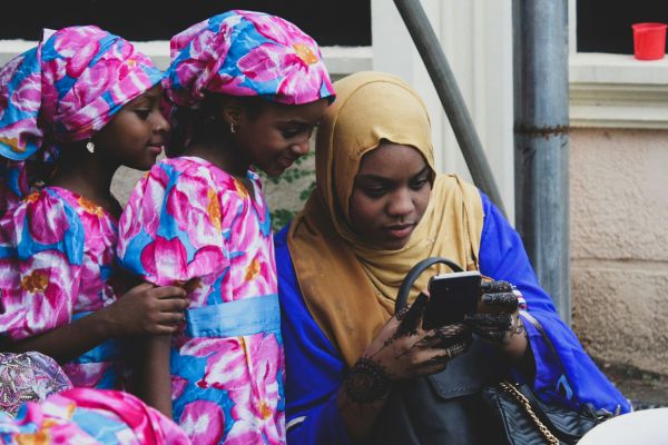 Three Nigerian girls huddle around a cell phone