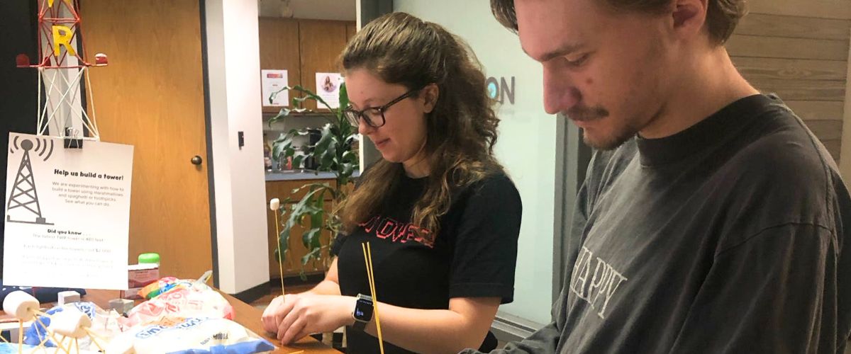 Veronica Jonas (left) and fellow TWR intern, Bryson Sappington (right), assist with testing another's internship project, assembling miniature radio towers out of spaghetti and marshmallows.