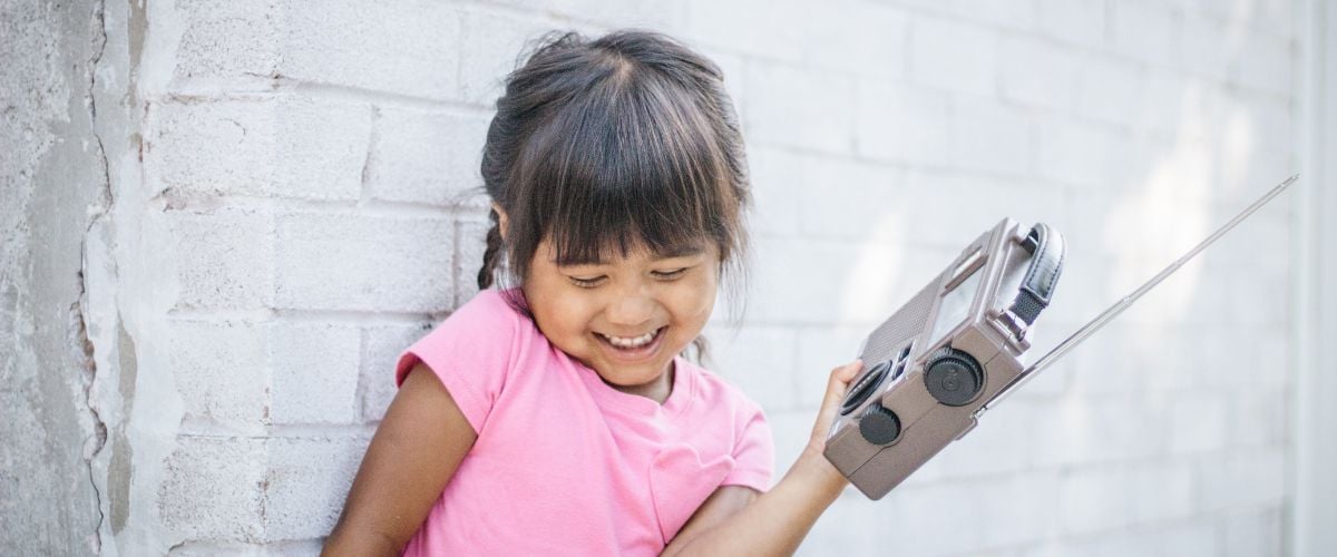 a little girl in a pink shirt laughs while holding a radio set in her hand